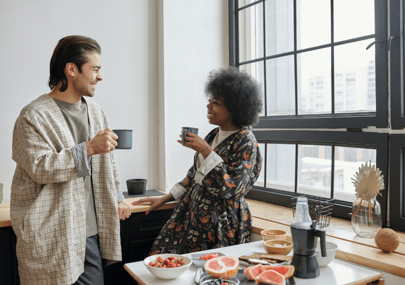 A couple having coffee and breakfast in front of a large window overlooking the city